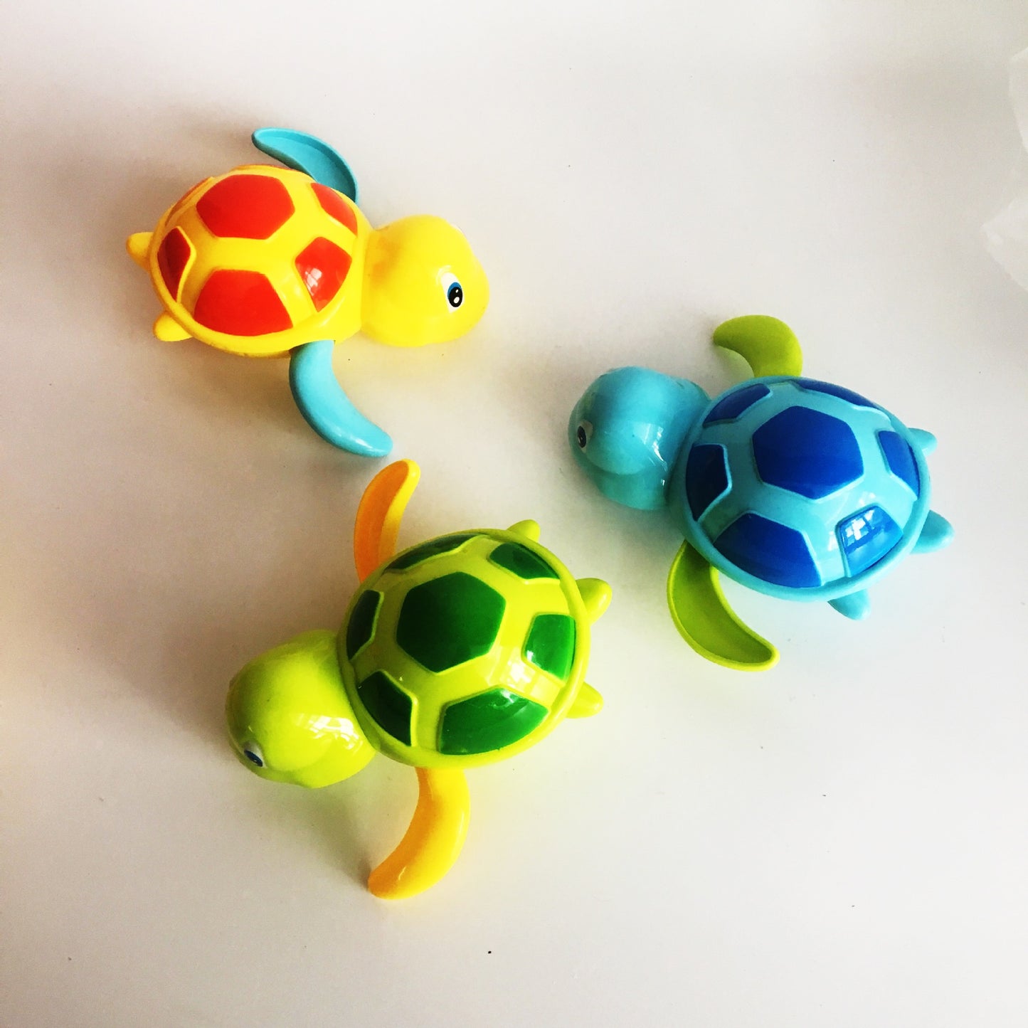Three colorful wind-up turtle toys in yellow, green, and blue, each with a patterned shell and playful, cartoon style.