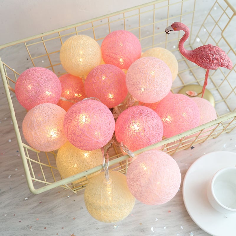 LED string lights with glowing pink and cream cotton-thread globes, inside a wire basket with a small flamingo figure.