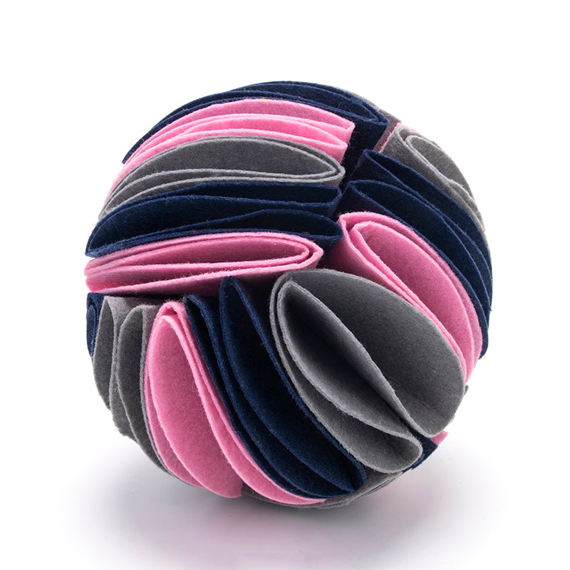Interactive dog snuffle ball made of layered felt fabric in pink, dark blue, and grey, isolated on white.