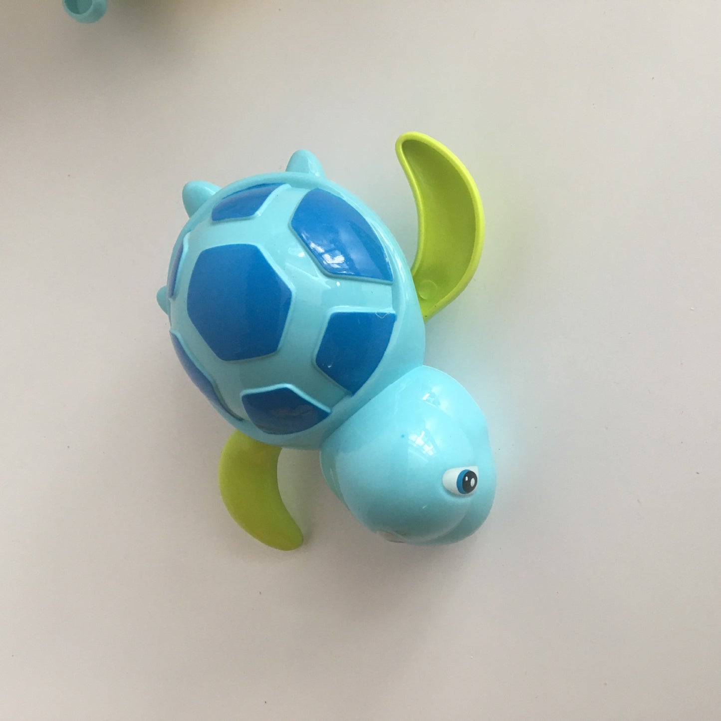 Light blue and navy plastic turtle wind-up toy with lime green flippers, viewed from above on a white surface.
