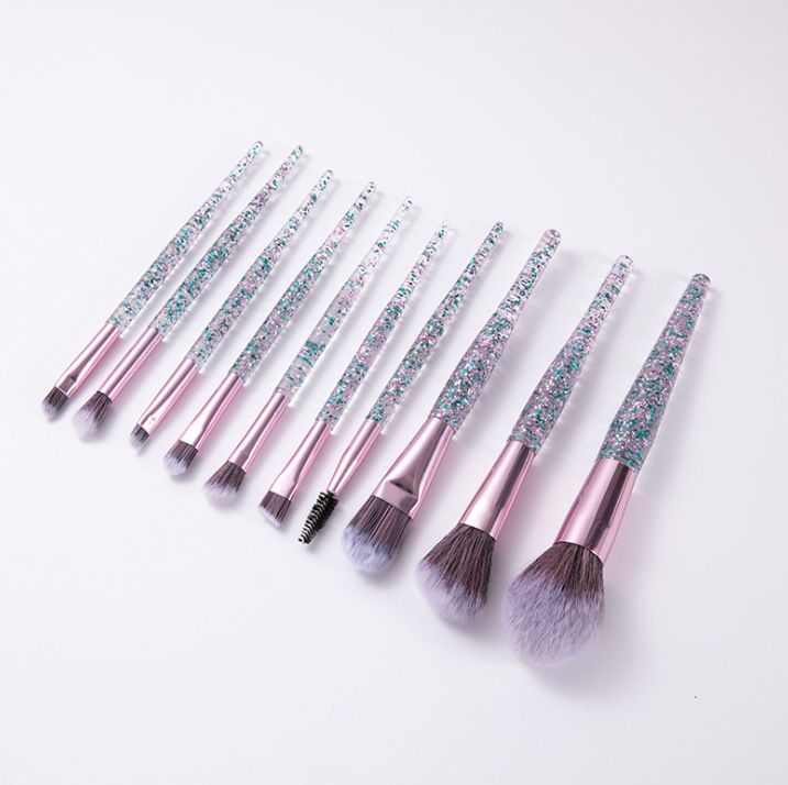 10-piece makeup brush set with clear handles filled with pink and green glitter, metallic pink ferrules, and soft tips.