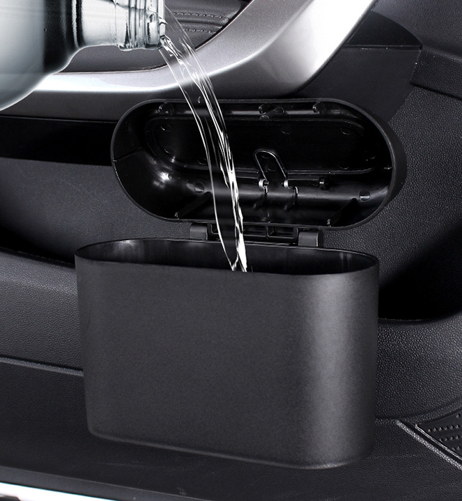 Black collapsible car trash bin mounted on a door panel, with water being poured into it from a plastic bottle.