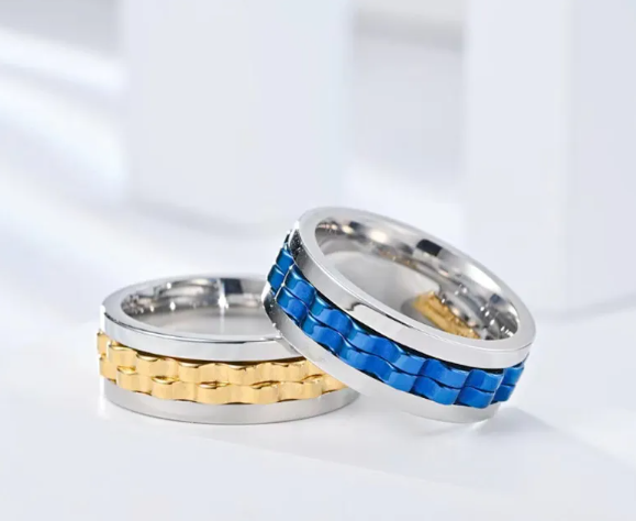 Two titanium steel fidget rings with a gear-shaped spinning center in metallic gold and vibrant blue.