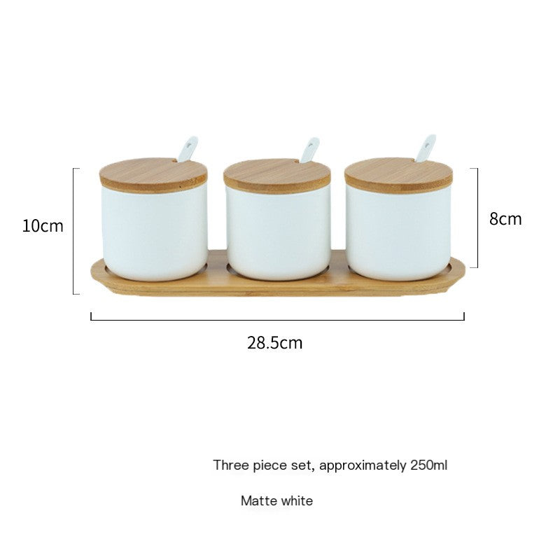 Three matte white ceramic spice jars with bamboo lids and spoons on a matching wooden tray, Nordic design style.