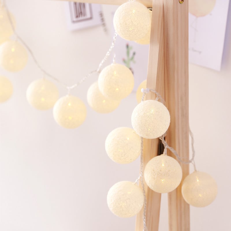 String of cream-colored, woven cotton LED globe lanterns draped over a light wooden frame, emitting a warm glow.