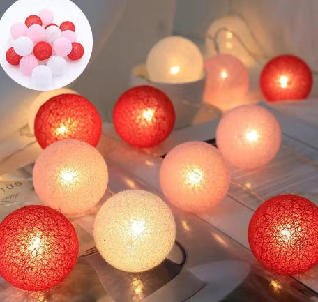 Cotton ball LED string lights in red, pink, and white glowing softly against a white table surface.