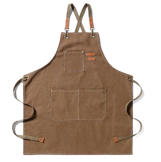 Brown canvas apron with crisscross straps, leather accents, brass hardware, and multiple front utility pockets.