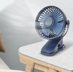 Navy blue portable USB clip-on desk fan with a round head, shown clipped to the edge of a light wood table.