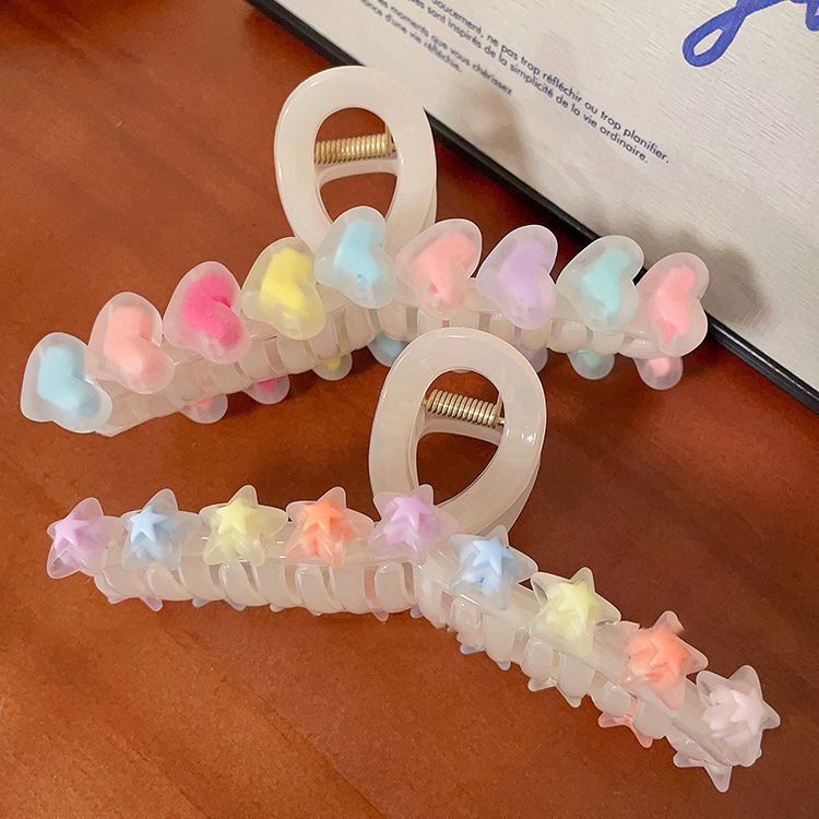 Two translucent cream claw clips, one decorated with pastel hearts and the other with pastel stars, on a wood surface.