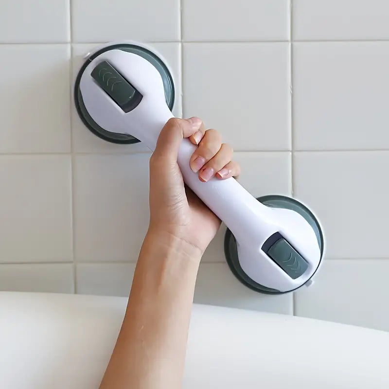 Hand holding a white and gray suction-cup safety grab bar attached to a tiled bathroom wall.