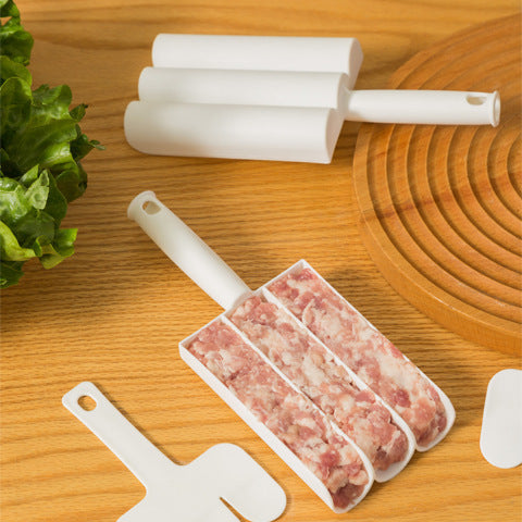 White plastic triple-slot meatball maker tool on a wooden table, filled with raw ground meat next to a spatula.