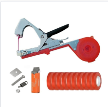 Red and silver garden plant tying tool with a tape dispenser, extra red tape rolls, staples, and small hardware parts.