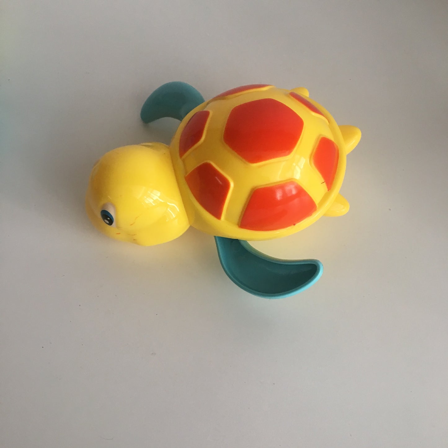 Yellow plastic turtle wind-up toy with a red-patterned shell and teal flippers on a plain white background.