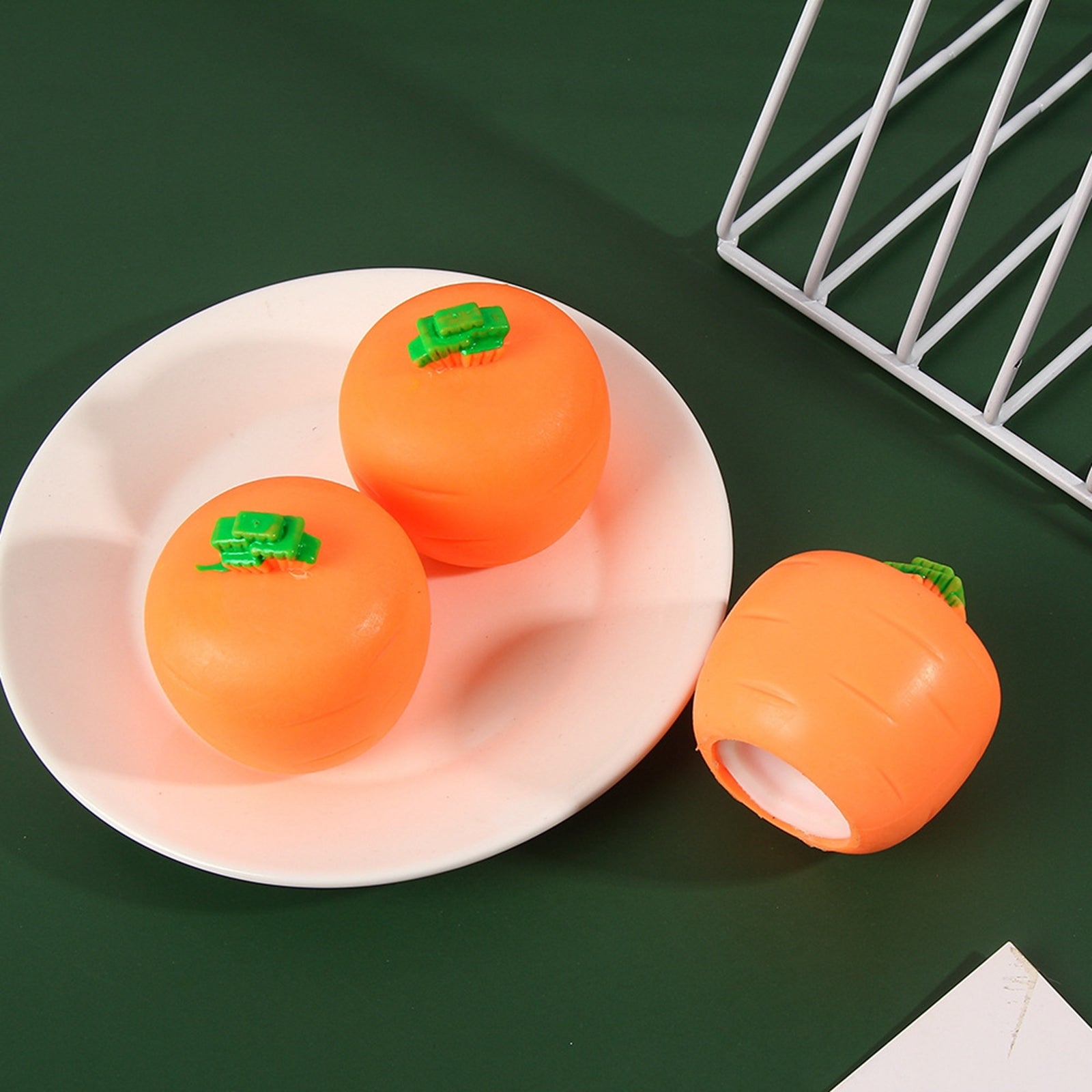 Three orange carrot-shaped squeeze toys with small green stems, two on a white plate and one beside it.