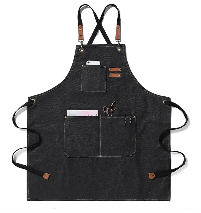 Black canvas apron with cross-back straps, brown leather accents, and multiple pockets holding tools and a phone.