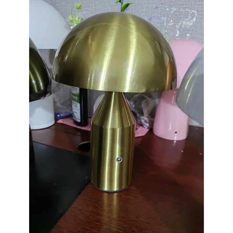 Minimalist brushed-gold metal mushroom desk lamp with a rounded dome shade and cylindrical base on a wooden table.
