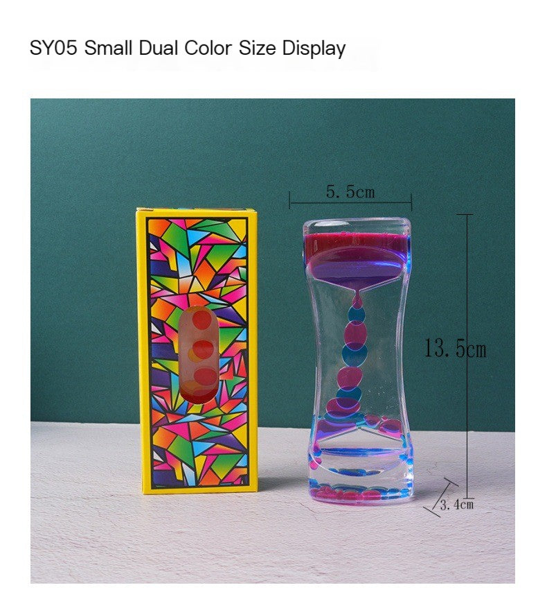 Acrylic liquid sand timer with pink and blue droplets beside a vibrant, geometric-patterned yellow storage box.