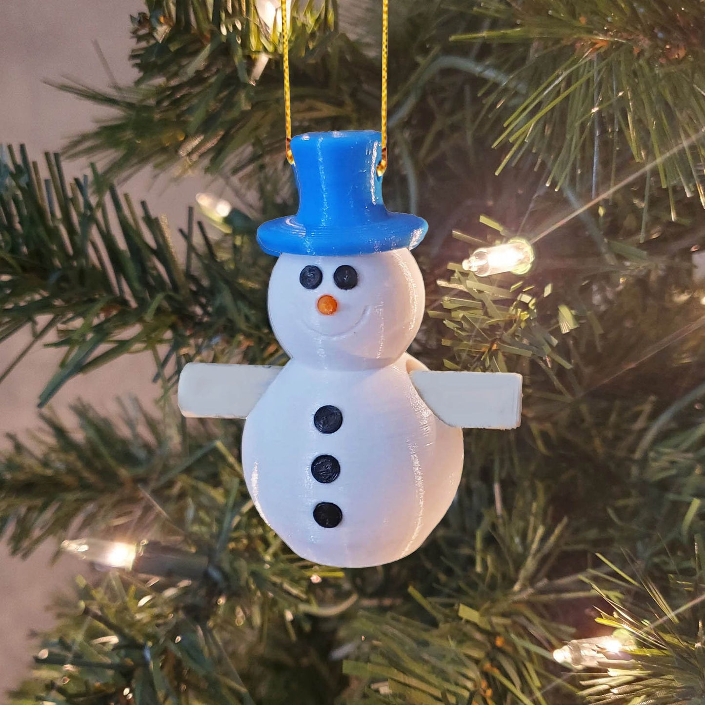 3D-printed white snowman ornament with a blue top hat and black buttons, hanging on a lit Christmas tree.