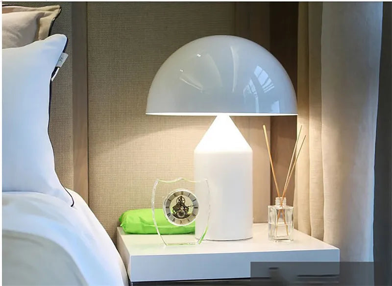 Modern white mushroom-shaped desk lamp glowing on a bedside table, next to a small glass clock and reed diffuser.