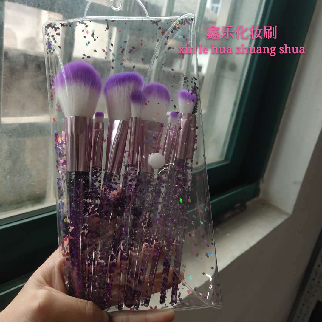 Ten-piece makeup brush set with purple and white bristles, rose gold ferrules, and clear handles filled with glitter.