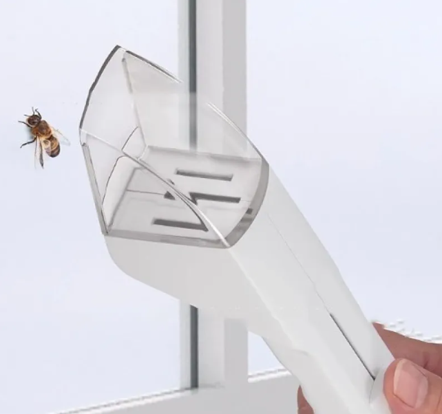 White portable bug catcher with a clear plastic head being used to gently capture a honeybee on a glass window.