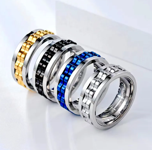 Four titanium steel gear fidget rings in gold, black, blue, and silver, arranged in a row on a white surface.