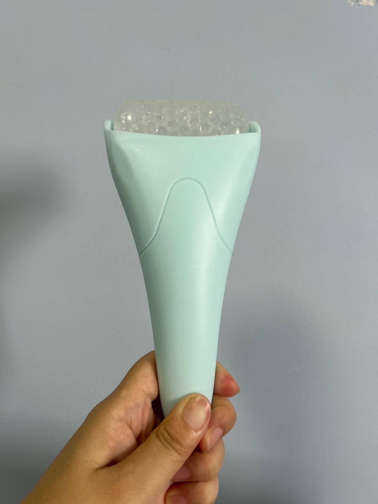 Light blue facial ice roller with a textured, bead-filled rolling head held in a hand.