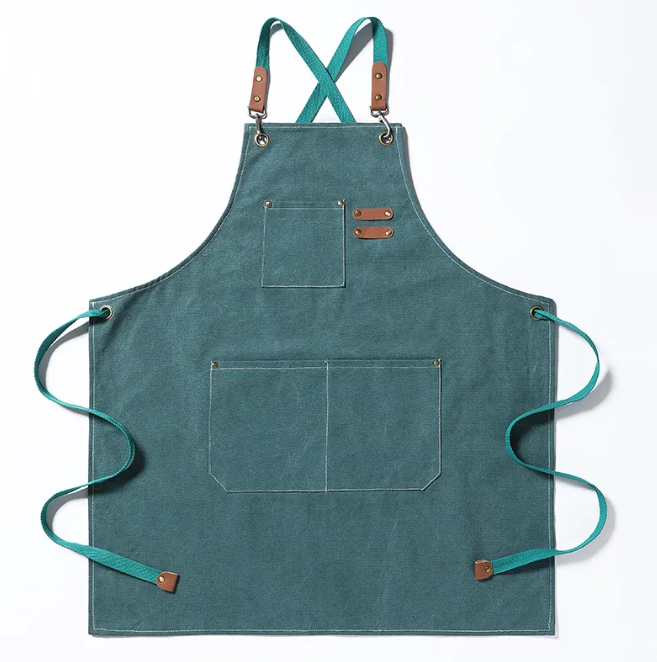 Teal canvas brewmaster apron with cross-back straps, tan leather accents, brass hardware, and multiple utility pockets.