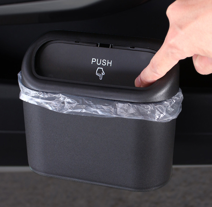 Small, matte black collapsible car trash bin with a "PUSH" lid, being opened by a finger.