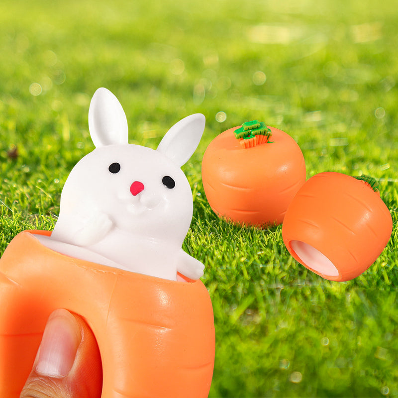 White bunny popping out of an orange carrot squeeze toy, with additional carrot shapes on a grassy background.