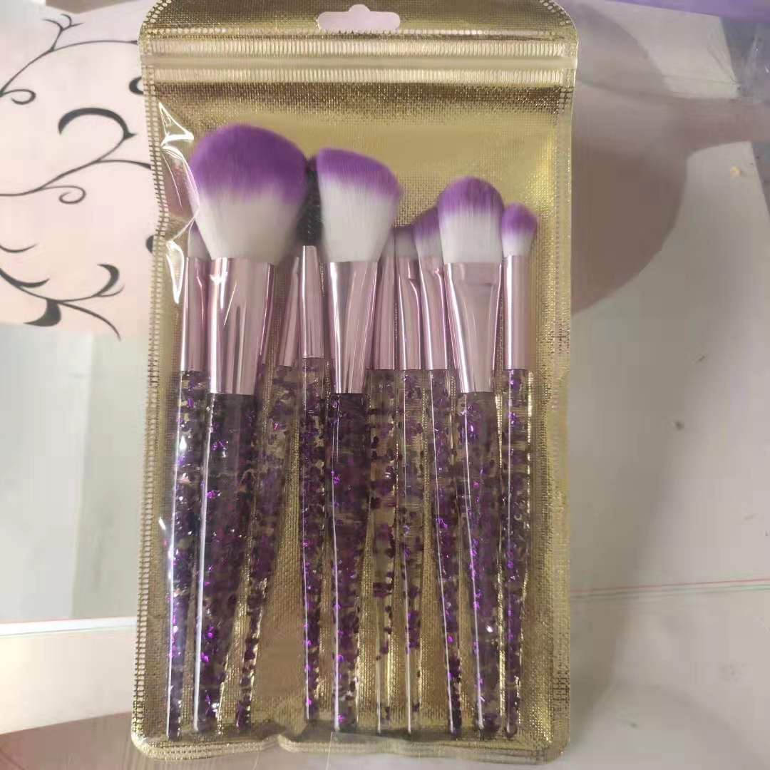 Ten-piece makeup brush set with purple-tipped bristles, rose gold ferrules, and clear handles filled with purple glitter.