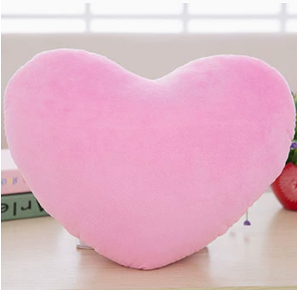 Soft pink heart-shaped plush pillow sitting on a desk.
