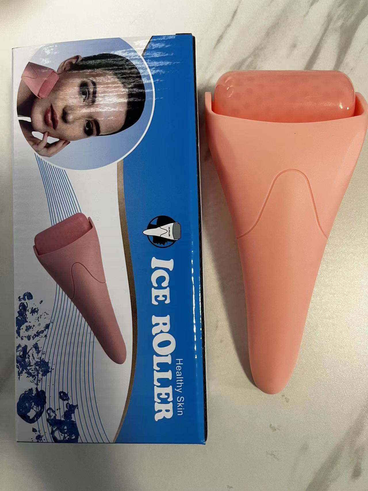 Light pink Chill Glide facial ice roller next to its blue and white retail box featuring a woman using the product.