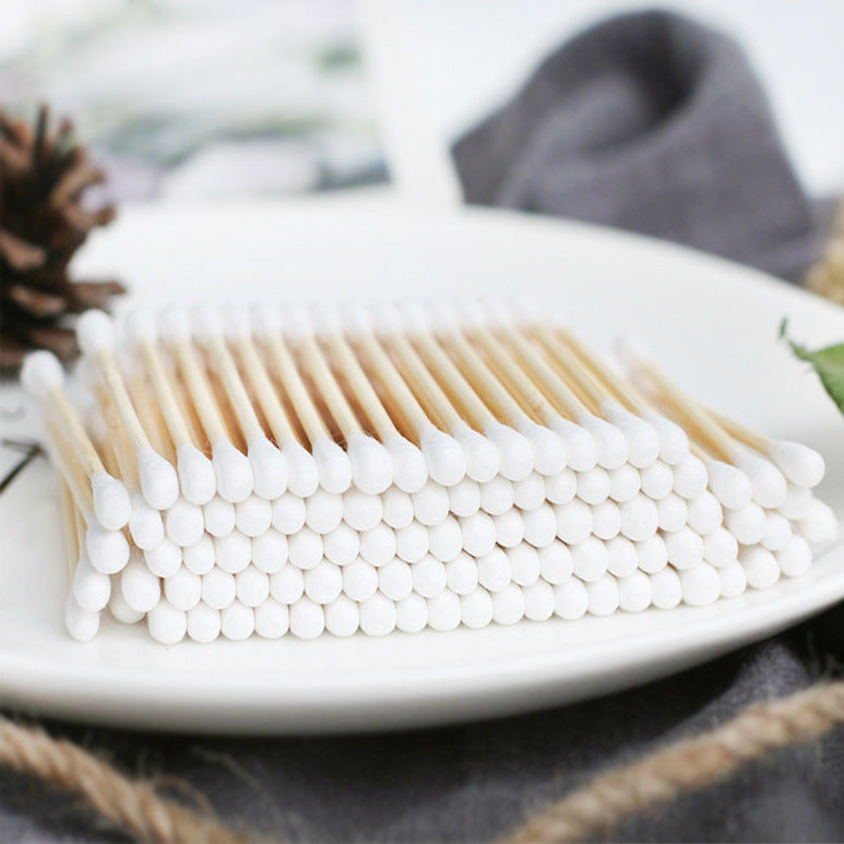 A neat stack of bamboo cotton swabs with white tips arranged on a white plate with rustic decor in the background.