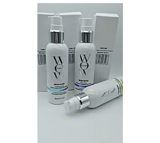Three white bottles of Color Wow Dream Cocktail leave-in hair treatment with silver pumps and boxes on a white surface.