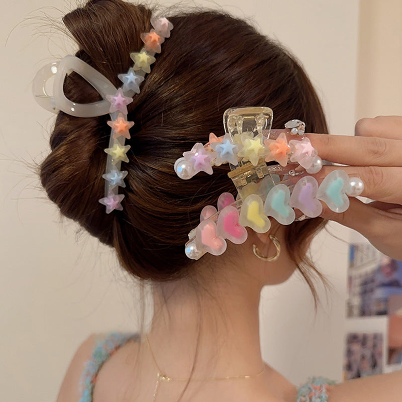 Clear claw clips decorated with pastel-colored stars and hearts, worn in a brown hair bun.