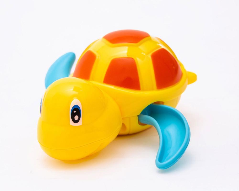 Bright yellow wind-up turtle toy with an orange shell pattern and blue swimming flippers on a white background.