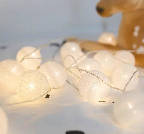 String of glowing, white cotton ball LED lanterns with a textured, spherical design against a soft, neutral background.
