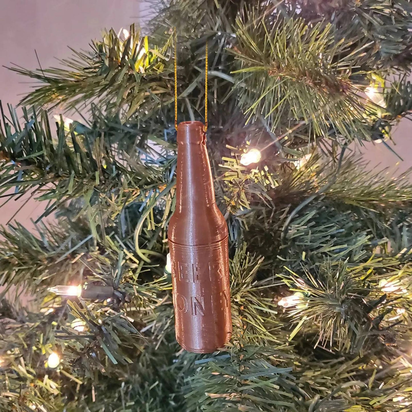 Brown beer bottle ornament hanging on a lit green Christmas tree with embossed "BEER ONLY" text.
