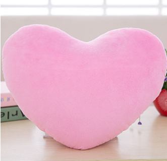 A soft, bright pink heart-shaped plush pillow sitting on a wooden surface.