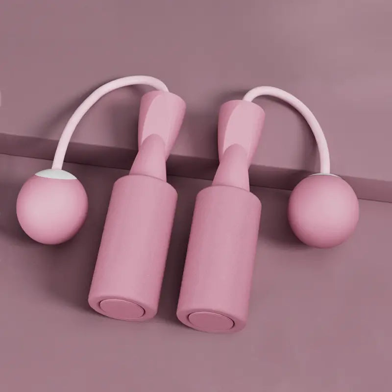 Dusty rose VersaRope cordless jump rope handles with attached weighted balls, featuring a minimalist matte finish.