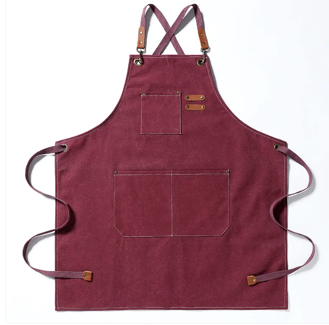 Maroon canvas apron with cross-back straps, bronze hardware, and multiple pockets for utility and style.