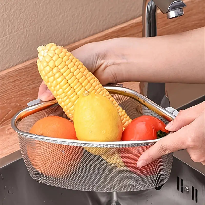Triangle stainless steel mesh sink strainer holding an ear of corn, a lemon, an orange, and a red bell pepper.