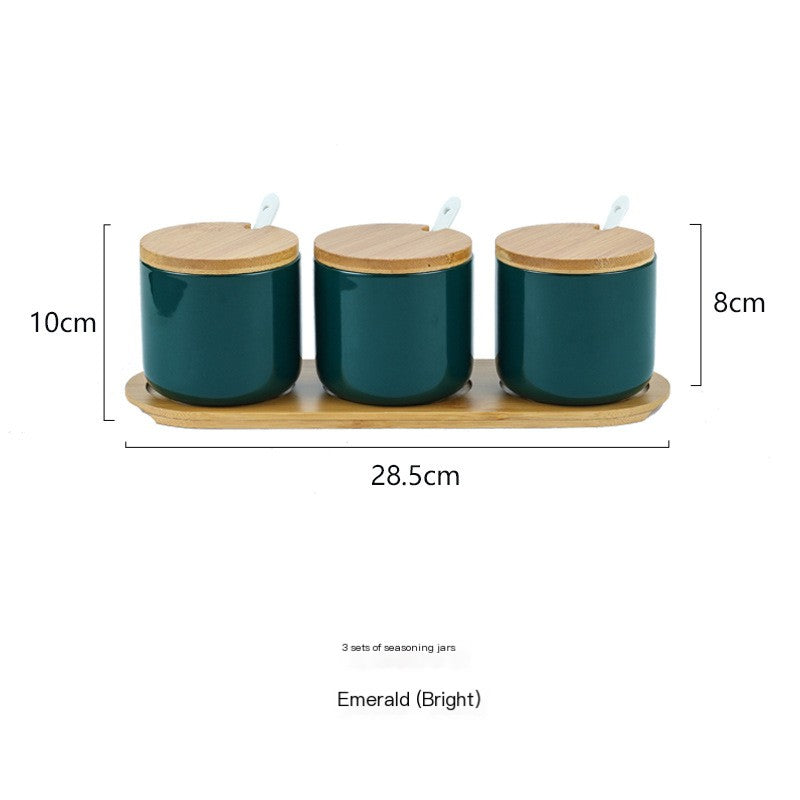 Three emerald ceramic spice jars with wooden lids and spoons on a matching wooden tray, featuring dimension labels.