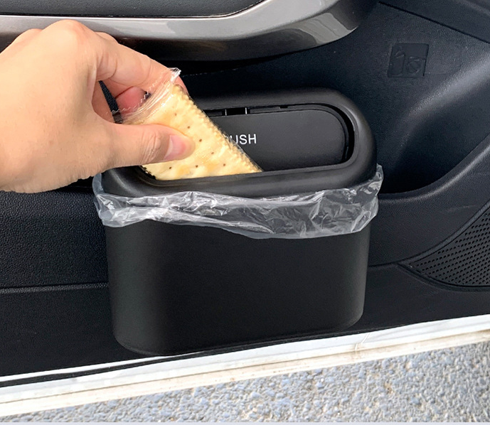 A hand deposits a cracker wrapper into a sleek, matte black collapsible car trash bin mounted on a door panel.