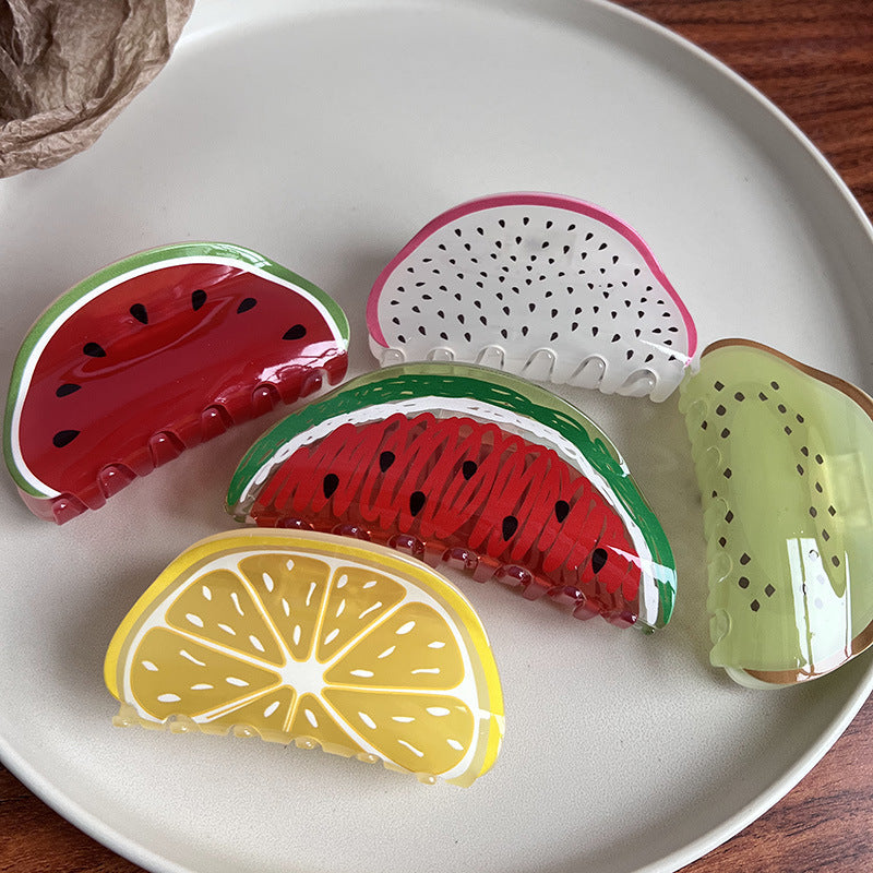Five glossy fruit-shaped acrylic hair claws: watermelon, lemon, kiwi, and dragon fruit, arranged on a white plate.