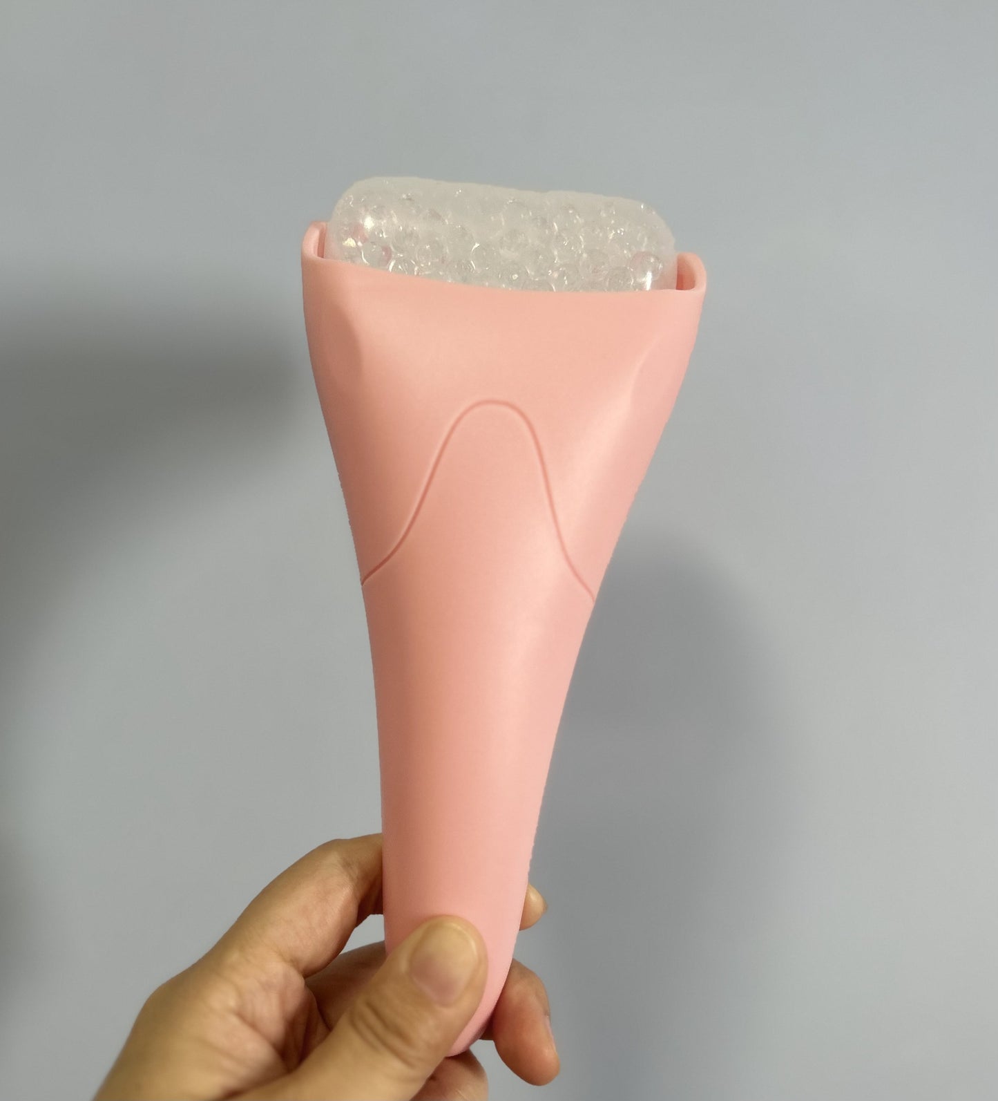 Chill Glide facial ice roller with a matte pink handle and a translucent, textured cooling drum against a gray wall.