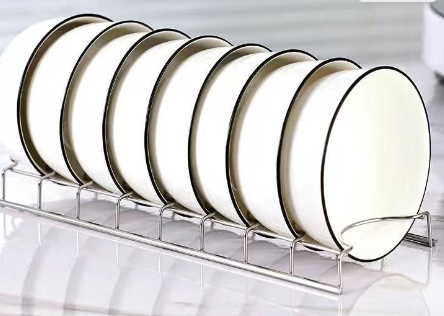 Sleek stainless steel wire rack holding a row of white bowls with black rim detailing.