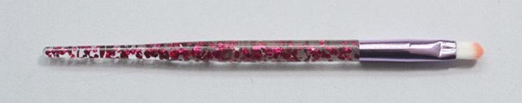 Makeup brush with a clear handle filled with red glitter, a metallic purple ferrule, and white bristles.