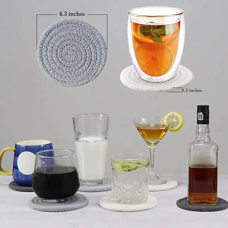 Round grey and white artisan woven cotton coasters supporting various glasses and a bottle, marked 4.3 inches wide.